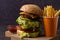 Homemade triple decker burger and fries on dark wooden background.