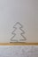 A homemade wire Christmas tree sits on a wooden shelf with white wallpaper symbolizing winter and snow.