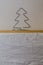 A homemade wire Christmas tree sits on a wooden shelf with white wallpaper symbolizing winter and snow.