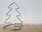 A homemade wire Christmas tree sits on a wooden shelf with white wallpaper symbolizing winter and snow.