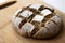 Homemade yeast sourdough rye wholegrain bread with Diamond Crosshatch scoring pattern on a wooden board with kitchen towel.