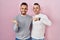 Homosexual couple standing over pink background amazed and smiling to the camera while presenting with hand and pointing with