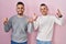 Homosexual couple standing over pink background smiling amazed and surprised and pointing up with fingers and raised arms