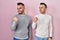 Homosexual couple standing over pink background smiling with happy face looking and pointing to the side with thumb up
