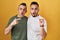 Homosexual couple standing over yellow background surprised pointing with finger to the side, open mouth amazed expression