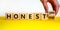 Honest symbol. Hand turnes a cube and changes the words `honest no` to `honest yes`. Beautiful yellow table, white background.
