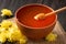 Honey with a dipper in a clay bowl and flowers on a dark wooden background