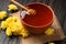 Honey with a dipper in a clay bowl and flowers on a dark wooden background