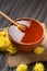 Honey with a dipper in a clay bowl and flowers on a dark wooden background