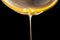 Honey dripping, pouring thick jet on black background. Viscous yellow honey molasses flowing. Close up of golden honey