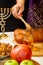 Honey drips from a wooden spoon in a woman`s hand next to the menorah challah and couscous and pomegranate