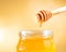 Honey jar on golden background with wooden dipper on top with drop honey