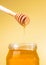 Honey jar on golden background with wooden honey dipper on top with drop honey