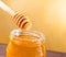 Honey jar on wood table and golden background with wooden dipper on top with drop honey