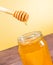 Honey jar on wood table and golden background with wooden honey dipper on top with drop honey