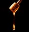 Honey stick with flowing honey over dark background close up