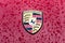 Hood emblem of sports car Porsche in raindrops on the burgundy background.