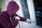 Hooded burglar forcing window to rob in the house