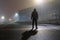 A hooded figure standing in the street in an empty industrial estate on a misty winters night