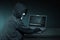 Hooded hacker with anonymous mask using laptop to steal data
