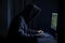 Hooded hacker using computer in dark room. Cybercrime concept, An anonymous hooded hacker full rear view coding on computer, AI