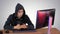 Hooded hacker using laptop and smartphone on gradient background.