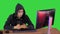 Hooded hacker using laptop and smartphone on a Green Screen, Chroma Key.