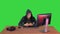 Hooded hacker using laptop and smartphone on a Green Screen, Chroma Key.