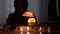 Hooded Shaman Boy Conjures over Pumpkin Candle in Dark Halloween Room