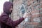 Hooded tagger writing graffiti on urban walls