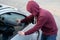 Hooded thief stealing a phone smart phone from a parked car