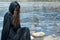 Hooded Woman with dark long hair in black robes in front of the Lake. Witches. Halloween and Gothic. Witchcraft and magic.