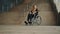 Hopeless young woman in the wheelchair in front of the inaccessible stairs.