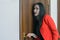 Horizontal close-up portrait of a woman in a red suit eavesdropping, spying on the door of the boss