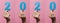 Horizontal collection of female hands holding and showing date 2020 cut out of cardboard on a colored pink background, concept new