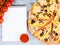 Horizontal food banner with cherry tomatoes, cutted pizza, spice and notebook on wooden background. Empty space for text.