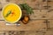 Horizontal image of bowl of carrot soup with rosemary garnish, spoon and toast on wood, copy space