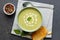 Horizontal image of bowl of pea soup with garnish, with toast and peppercorns on slate