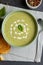 Horizontal image of bowl of pea soup with garnish, with toast and peppercorns on slate