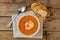 Horizontal image of bowl of tomato soup with spoon and toast on wooden table