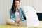 Horizontal indoor image of smiling young woman sitting on the bed and unpacking the parcel. Surprised female receive a gift box