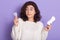 Horizontal indoor shot embarrassed pretty brunette looking at menstrual cup, holding hygiene napkin and menstrual cup in both