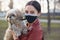 Horizontal outdoor shot of good looking careful brunette in mask being outside during quarantine, having walk with favourite pet,