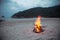 Horizontal outdoors shot of blazing campfire on sand at the seaside.