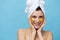 Horizontal photo, a woman with clean skin on a blue background with a towel on her head and body takes care of her face