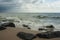 Horizontal photography of foaming sea water. Big wave on the empty shore. Wet sand on the beach. Big wet stones on the shore