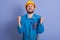 Horizontal picture of exhausted construction worker clenching his fists, raising hands, closing eyes, being tired of work, wearing
