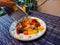 Horizontal picture: grating hard cheese over a plate of vegetarian meal in a garden