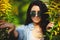 Horizontal portrait of beautiful woman in round sunglasses peeps out among yellow flowers.