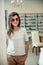 Horizontal portrait of charming young european female customer standing in optician store, trying stylish pair of